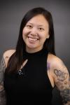 Asian woman with short brown hair and a lot of arm tattoos wearing a black shirt