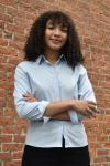 Person with folded arms stands in front of brick wall.