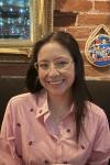 woman with dark hair with glasses and a striped shirt smiling