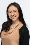 woman with dark hair and glasses in a tan shirt smiling