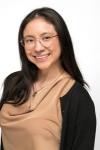 woman with dark hair and glasses in a tan shirt smiling