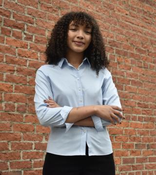 Person with folded arms stands in front of brick wall.