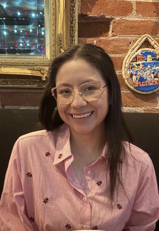 woman with dark hair with glasses and a striped shirt smiling
