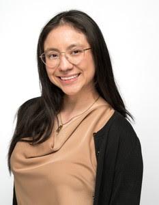 woman with dark hair and glasses in a tan shirt smiling